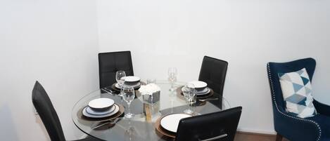 A dining area with a round glass table, black chairs, and a blue chair with a patterned cushion.