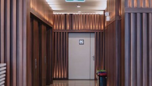 A hallway with a shiny tiled floor, wooden paneling on the walls, and a door with an emergency exit sign. - Marlen Hotel Denizli (Denizli)