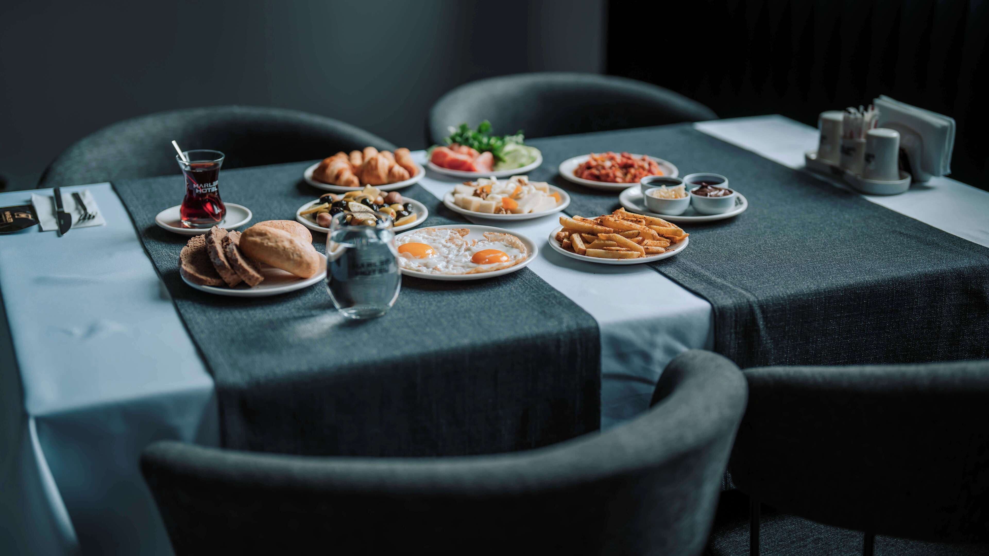 A dining table with various dishes, including croissants, eggs, and fries, set on a table with a dark tablecloth.