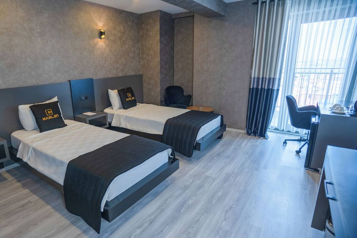 A modern hotel room with two beds, a desk, and a chair.