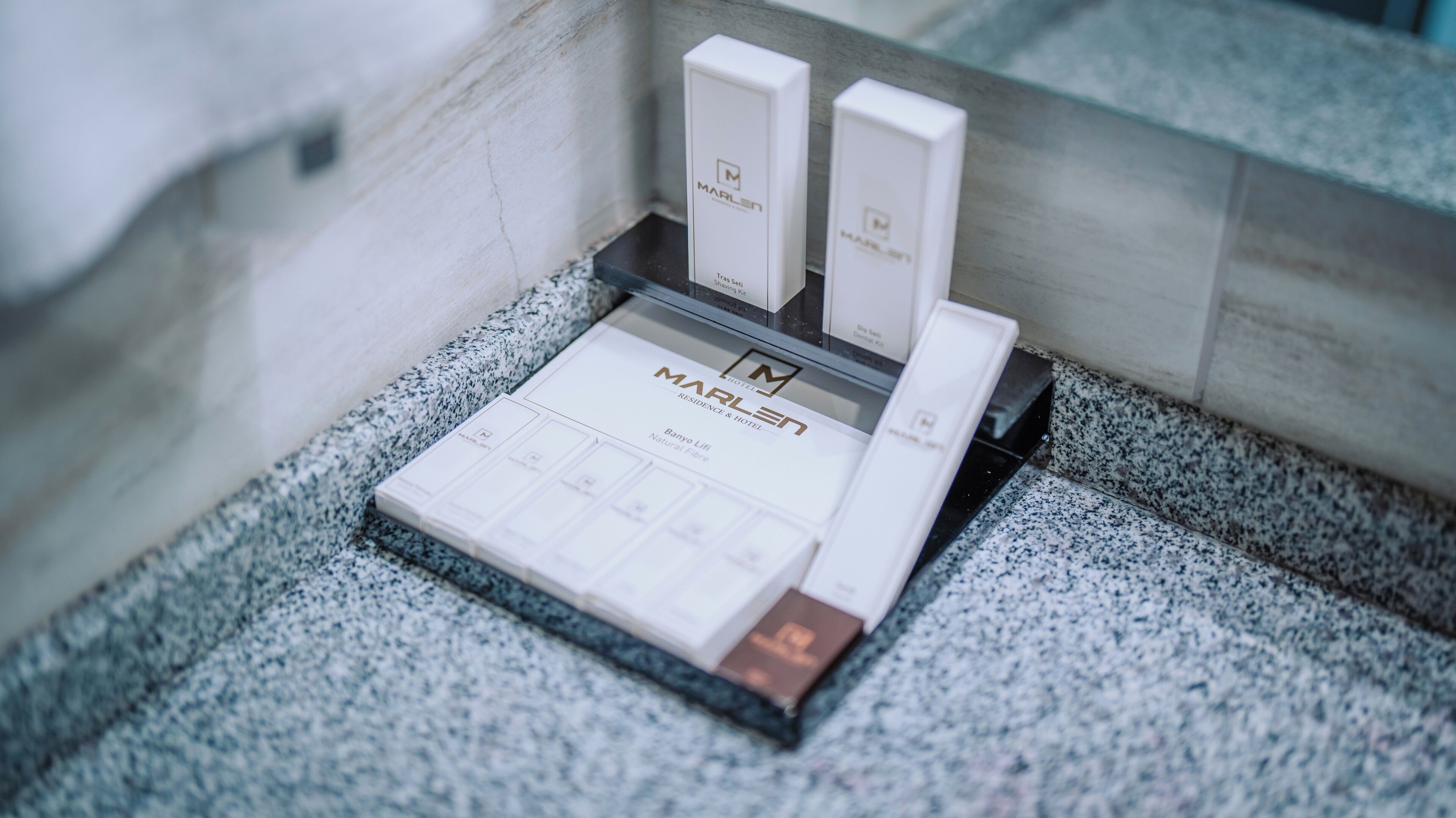 A brochure stand with a MARLEN brochure and two boxes, likely for hotel services, on a granite countertop.