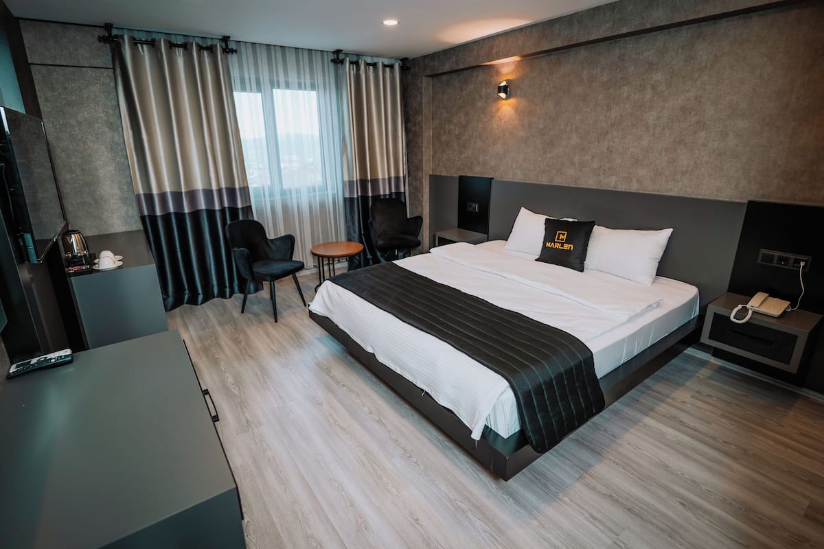 A modern hotel room with a large bed, a desk, a chair, and a bedside table with a phone.