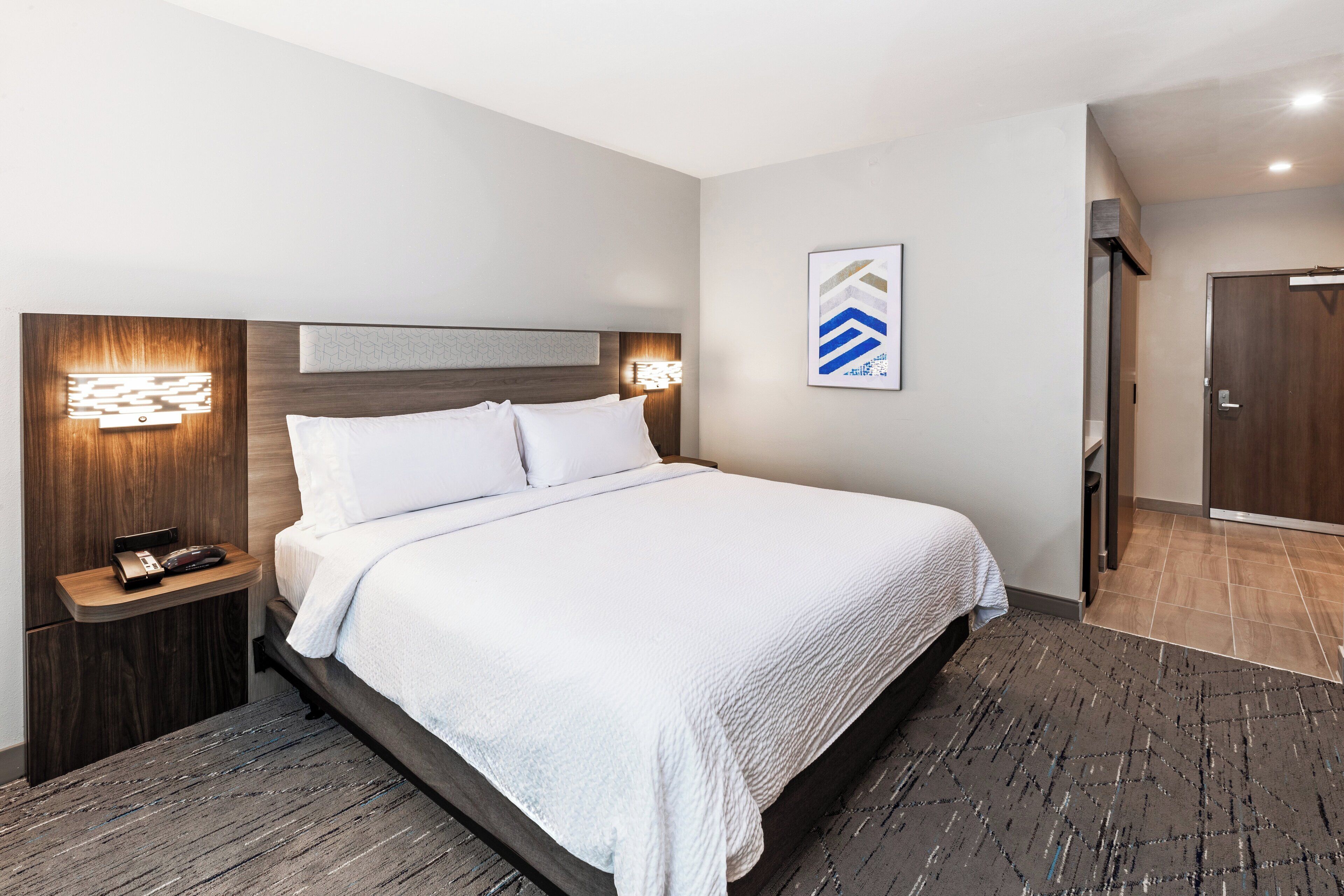 Une chambre d’hôtel moderne avec un grand lit, une table de chevet avec un téléphone et un luminaire fixé au mur.