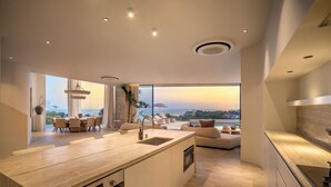A modern kitchen with a large island, a dining area with a view, and a cozy seating area. - Villa Namiko by Alfred in Bali (Pecatu)