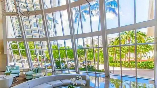A modern hotel lobby with a large glass window, a curved white sofa, and a round coffee table. - New Cozy Apt w/ Luxury Amenities & Amazing Views (Hallandale Beach)