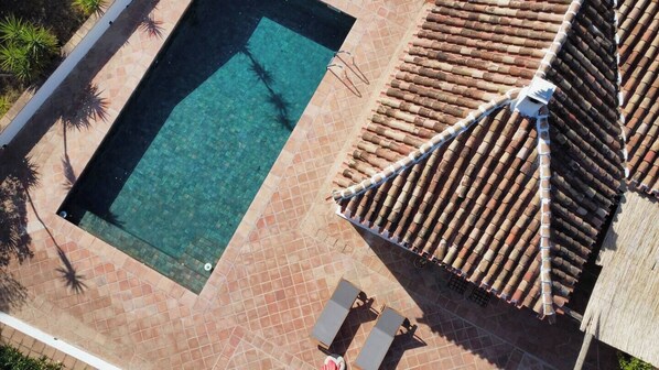 Vista aérea de una piscina con suelo y techo de baldosas, y una pequeña estructura con techo.