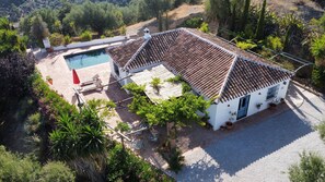 Una villa blanca con techo de tejas, piscina y jardín con diversas plantas.