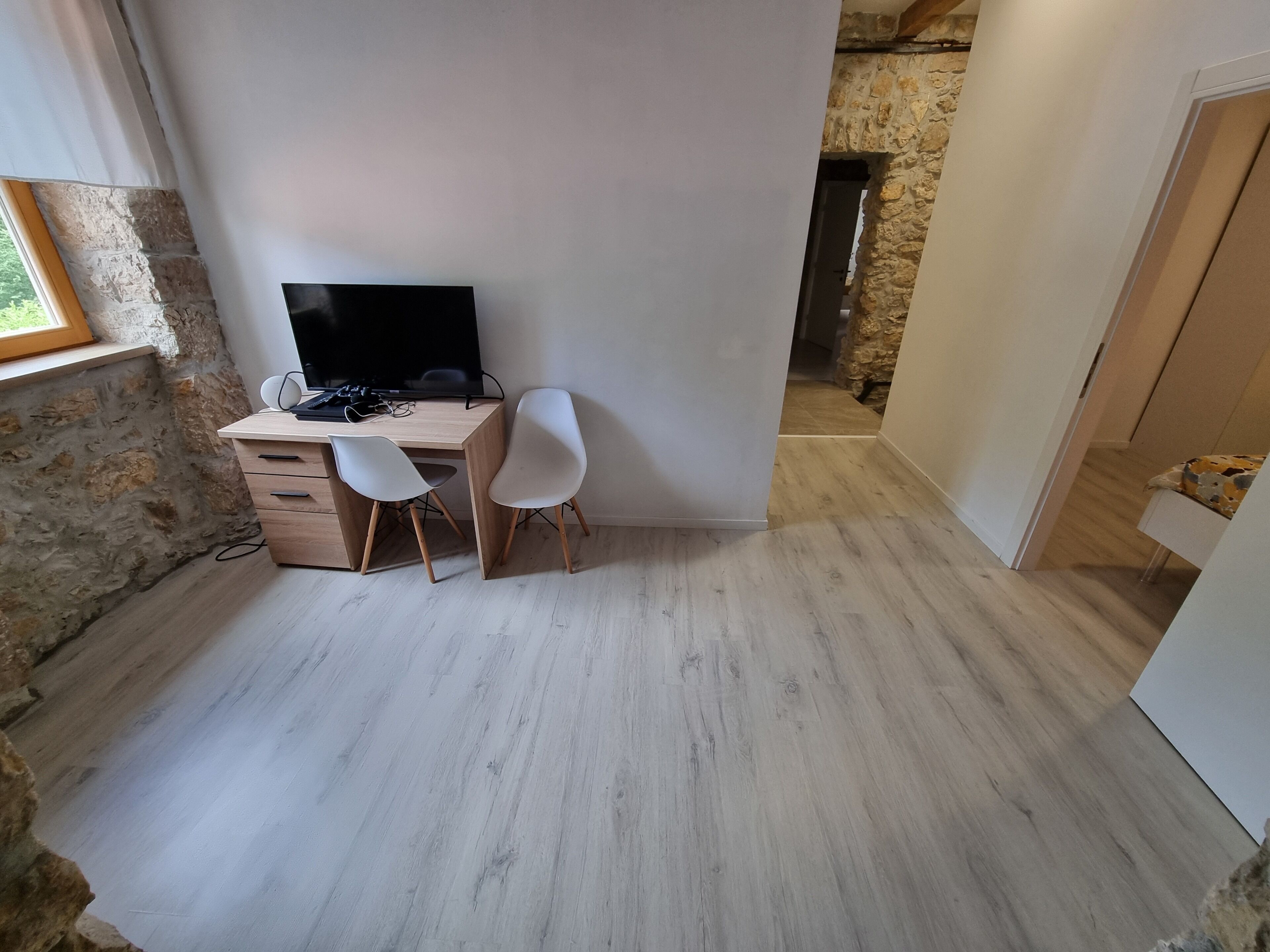 Una habitación pequeña y moderna con un escritorio de madera, dos sillas blancas, un televisor de pantalla plana y una pared de piedra.