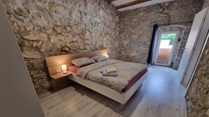 Camera da letto con parete in pietra, testiera in legno, comodino con lampada e letto con copripiumino fantasia.
