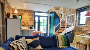 Un salon chaleureux avec un canapé bleu, un escalier en bois et un coin cuisine.