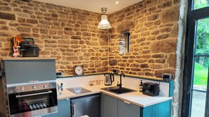 Une cuisine compacte avec un mur en pierre, un four encastré, un évier et une petite fenêtre.