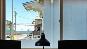 Vista per la finestra d'un carrer amb edificis, una platja i un fanal al primer pla.