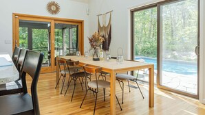 A dining area with a wooden table and chairs, a vase with dried flowers, and a view of a swimming pool through large glass doors. - Cold Spring Mountain Retreat: Secluded Oasis (Cold Spring)