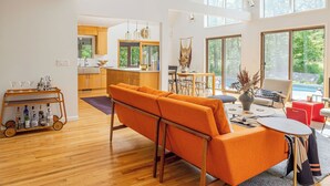 A spacious living area with a modern orange sofa, a dining table, and a kitchen in the background. - Cold Spring Mountain Retreat: Secluded Oasis (Cold Spring)