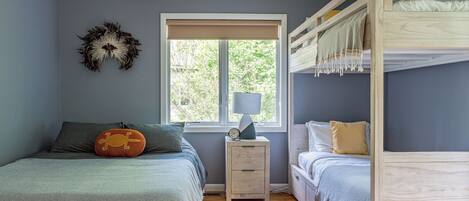 A bedroom with a bunk bed, a bedside table with a lamp, and a window with a view of trees.