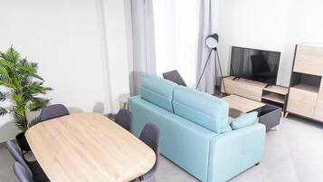 Una sala moderna con un sofá azul claro, una mesa de comedor de madera y un televisor.