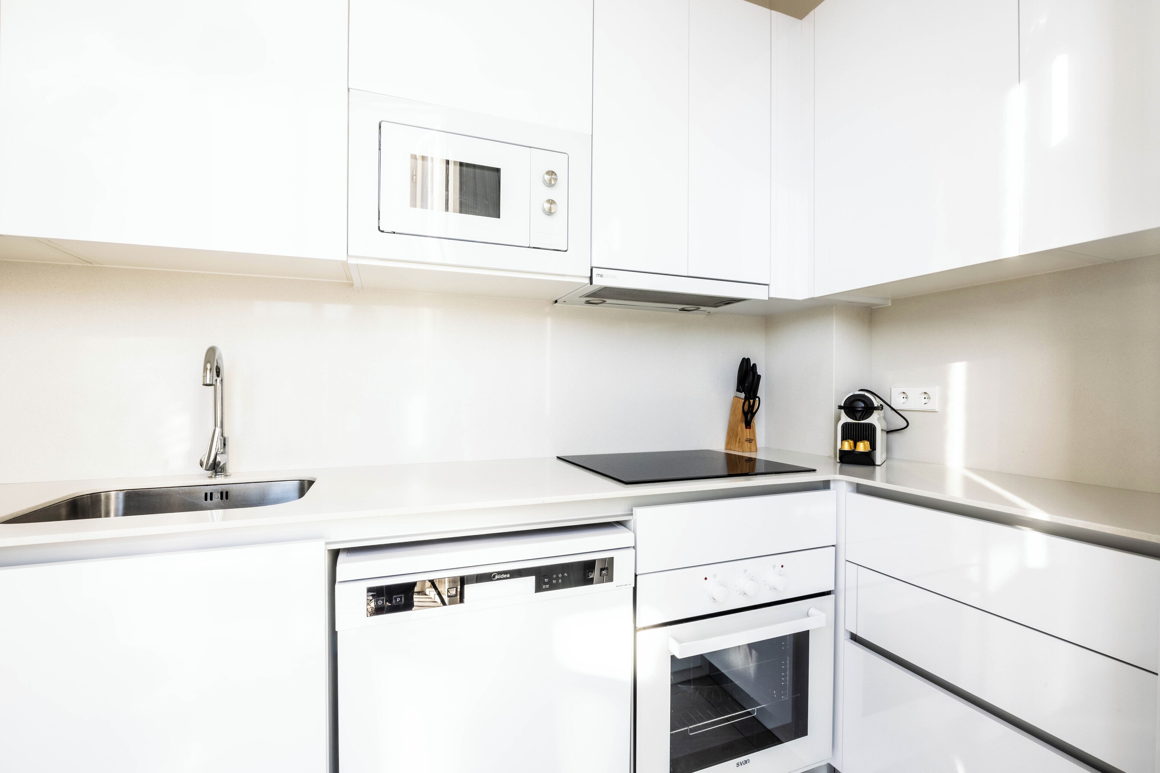 A modern kitchen with white cabinetry, a built-in microwave, a dishwasher, and a stove.