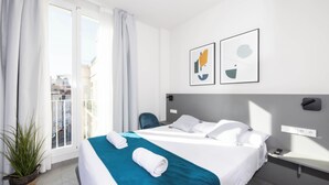 Una camera d'albergo con un letto, un comodino, una pianta in vaso e una finestra con tende.