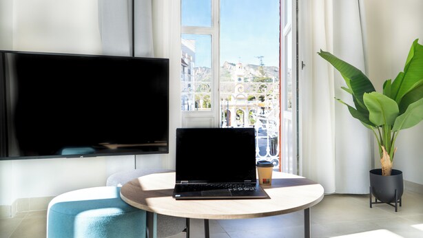 Una stanza con un laptop su un tavolo rotondo, una TV a parete e una pianta in vaso.