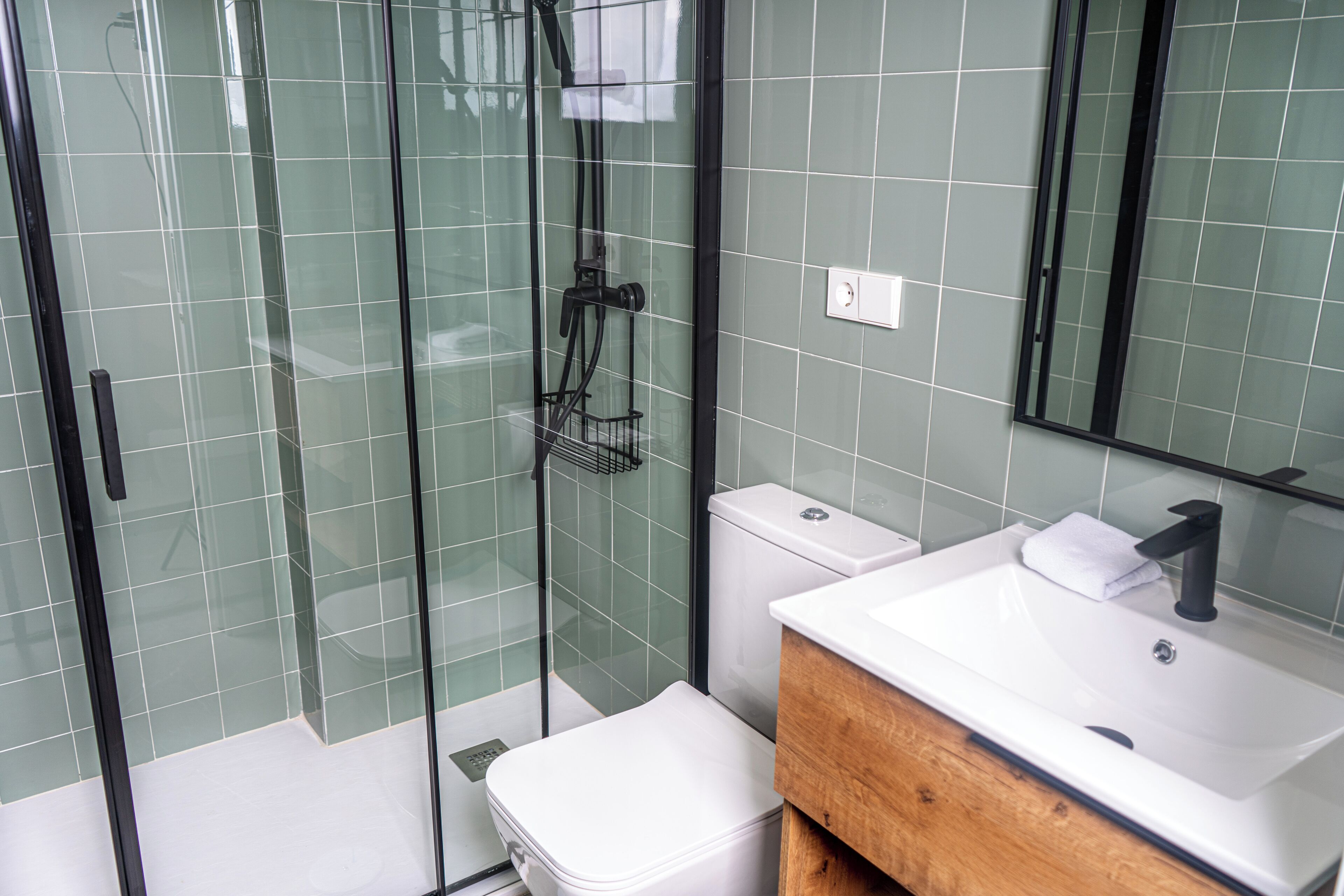 Un baño moderno con ducha de vidrio, inodoro blanco y tocador de madera con lavamanos.
