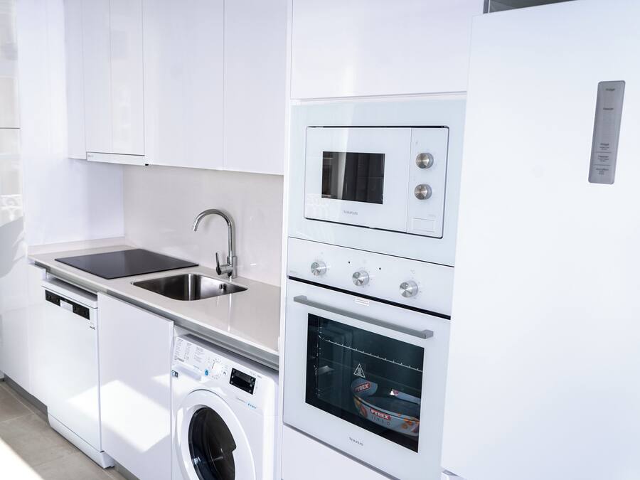 Una cocina moderna con armarios blancos, lavavajillas integrado, lavadora, microondas y horno.