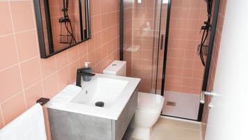 Un baño moderno con un lavabo blanco grande, un inodoro y una cabina de ducha con paredes de vidrio.