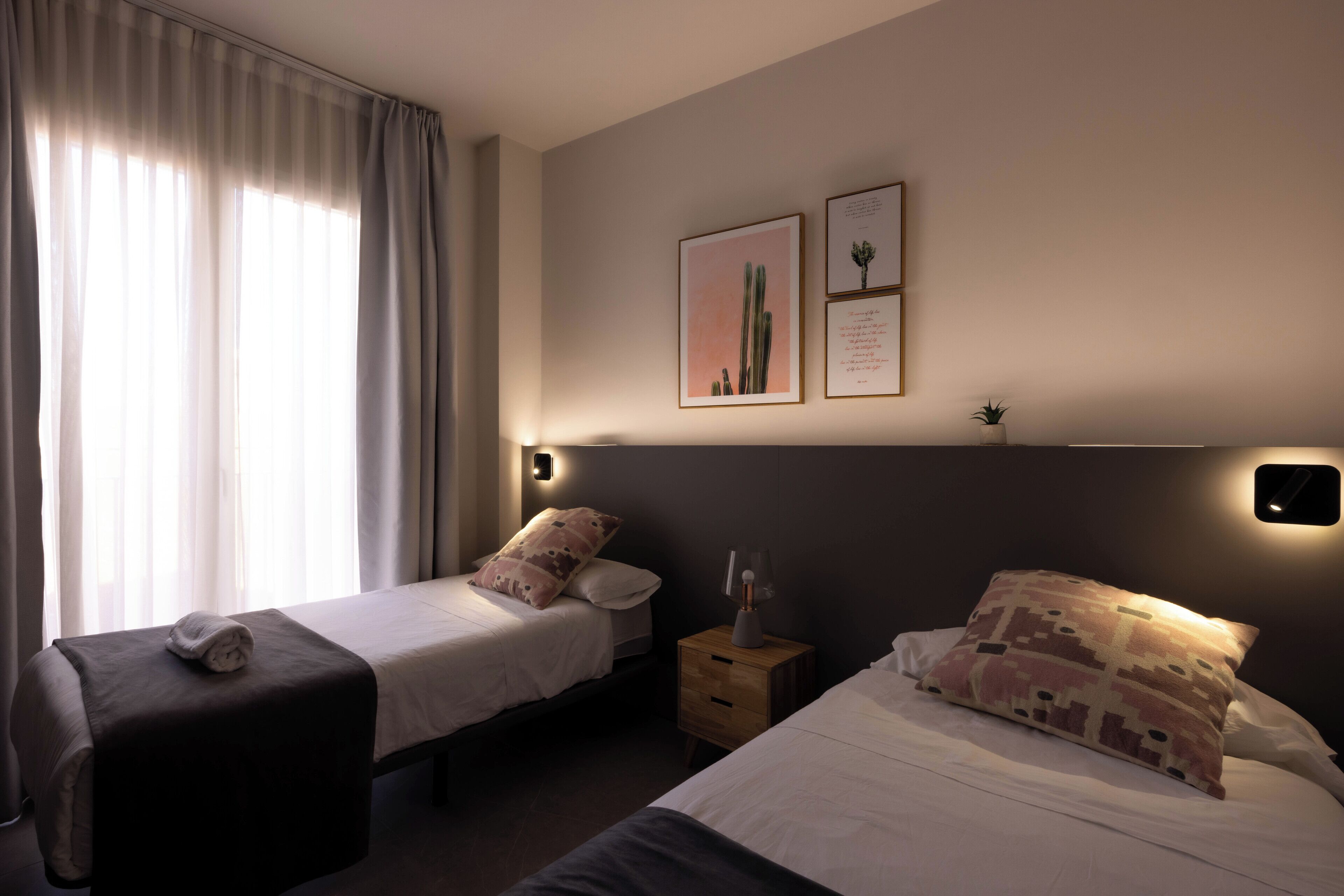 Una habitación de hotel con dos camas, una mesita de noche con lámpara y una luz en la pared.