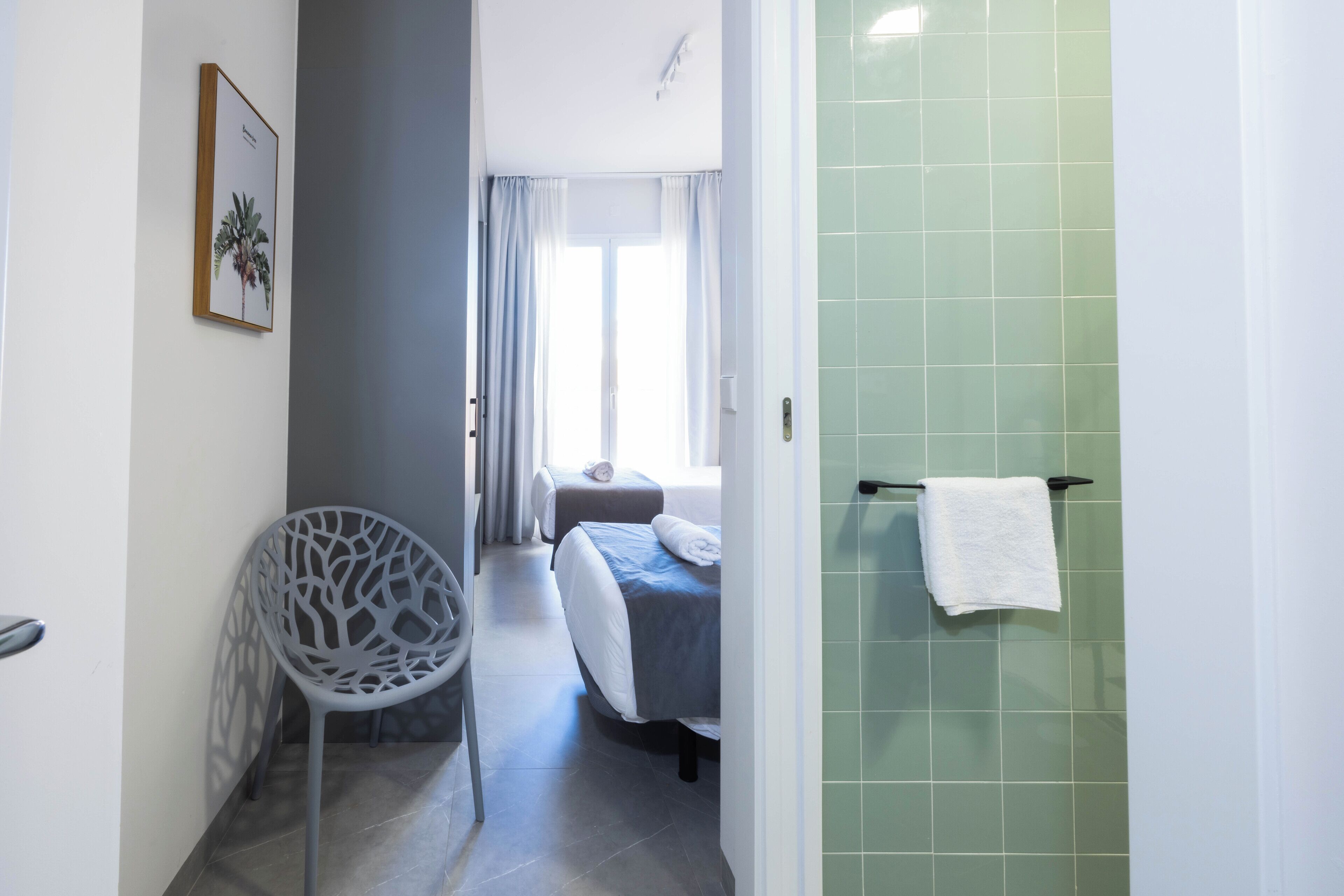 Habitación de hotel con cama, una silla, baño con toallero y un cuadro en la pared.