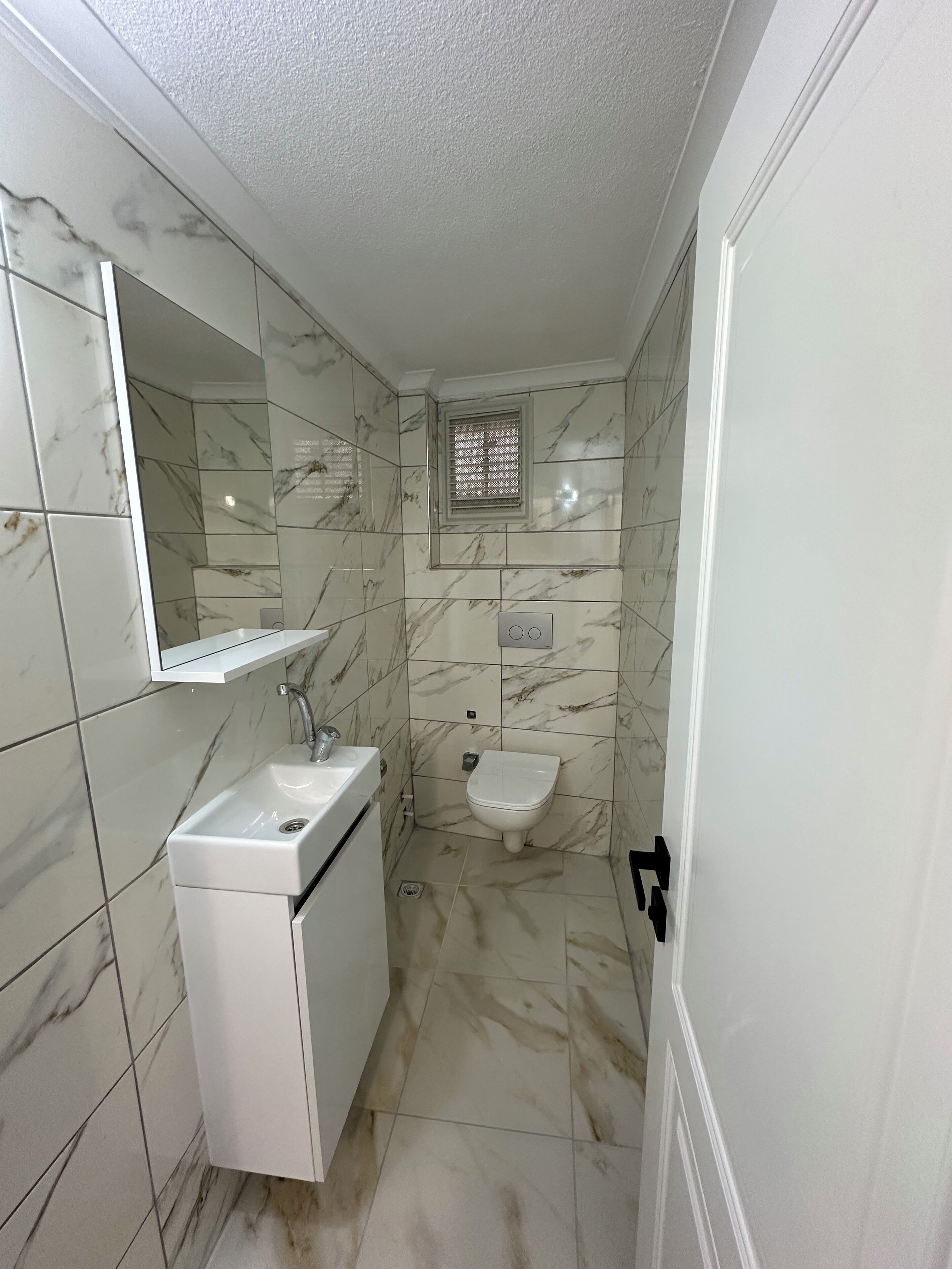 Une salle de bain avec un lavabo blanc, un miroir, des toilettes et une fenêtre avec des stores.