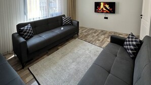 A modern living room with a sofa, a television, and a fireplace on the wall. - ÖZTÜRK VIP (Trabzon)