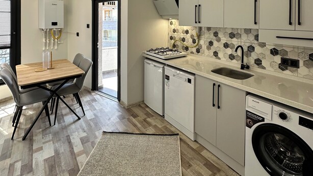 A modern kitchen with white cabinets, a built-in stove, a dishwasher, and a washing machine. - ÖZTÜRK VIP (Trabzon)