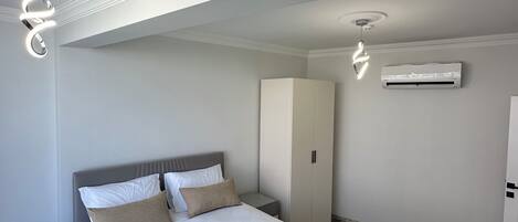 Quarto de hotel moderno com uma cama bem arrumada, mesa de cabeceira, guarda-roupa e ar condicionado.