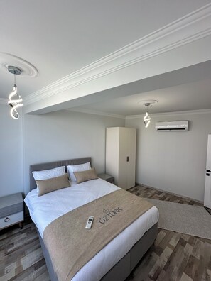 A modern hotel room with a neatly made bed, a bedside table, a wardrobe, and an air conditioning unit.