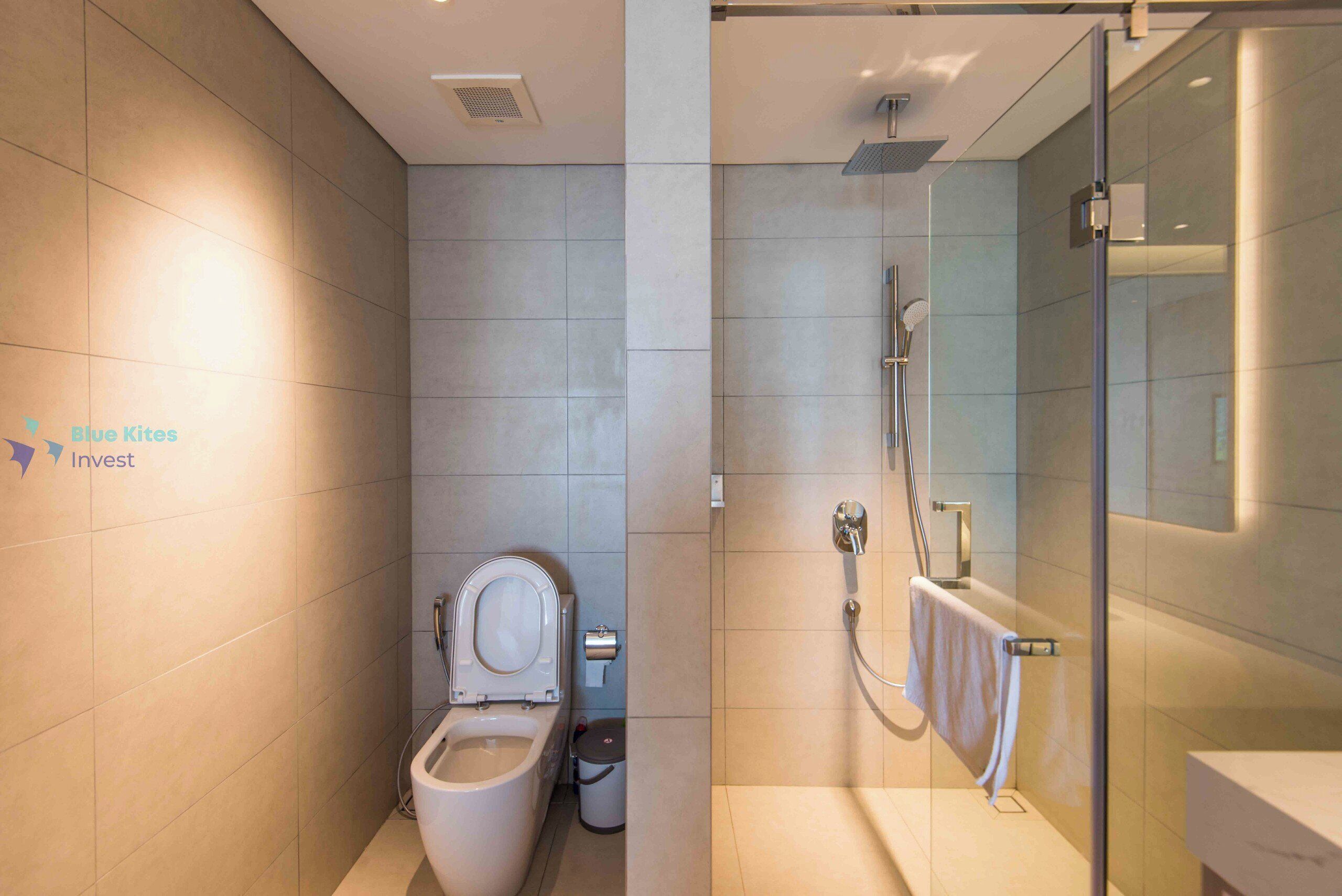 Une salle de bain moderne équipée de toilettes, d’une douche et d’un espace douche clos par des parois de verre.