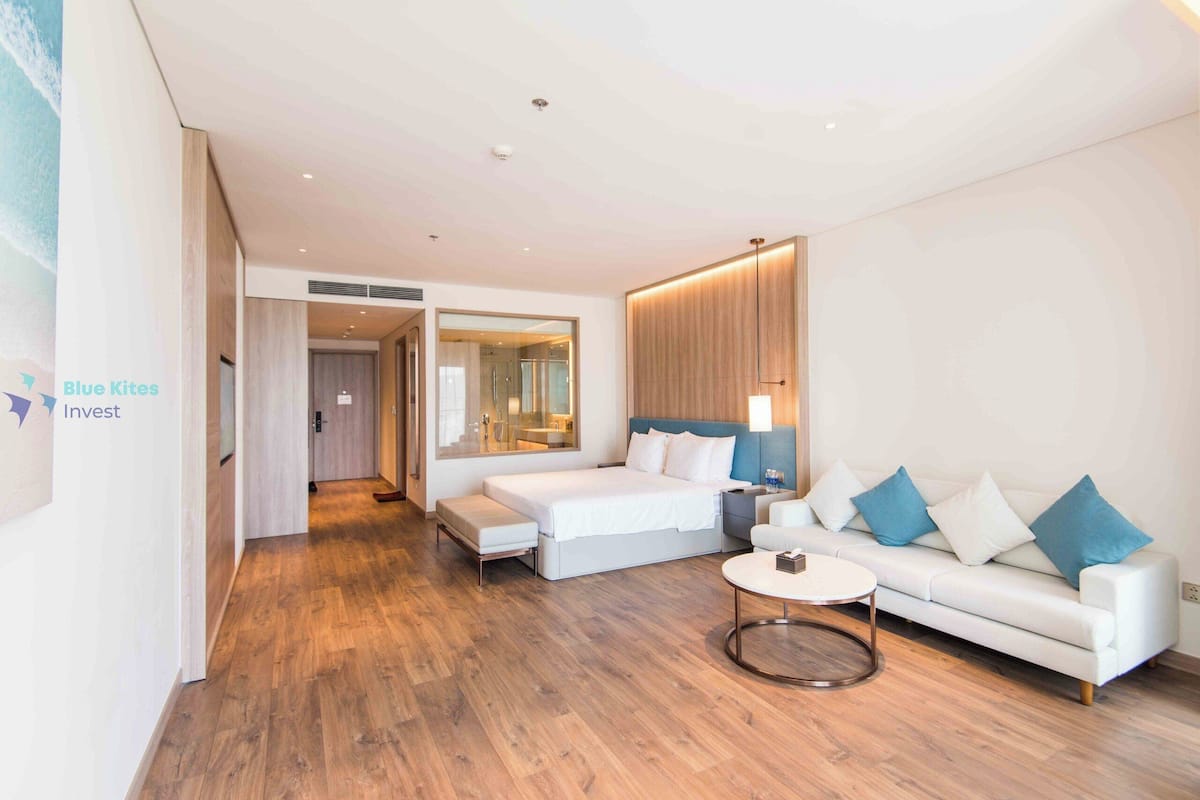 Une chambre d’hôtel moderne avec un grand lit, un canapé, une table basse ronde et un miroir.