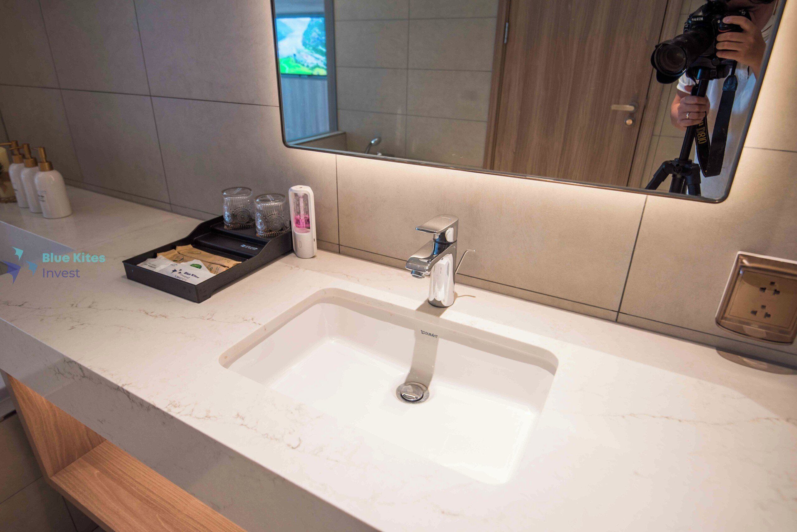 A modern bathroom with a large sink, a mirror, and toiletries on the counter.