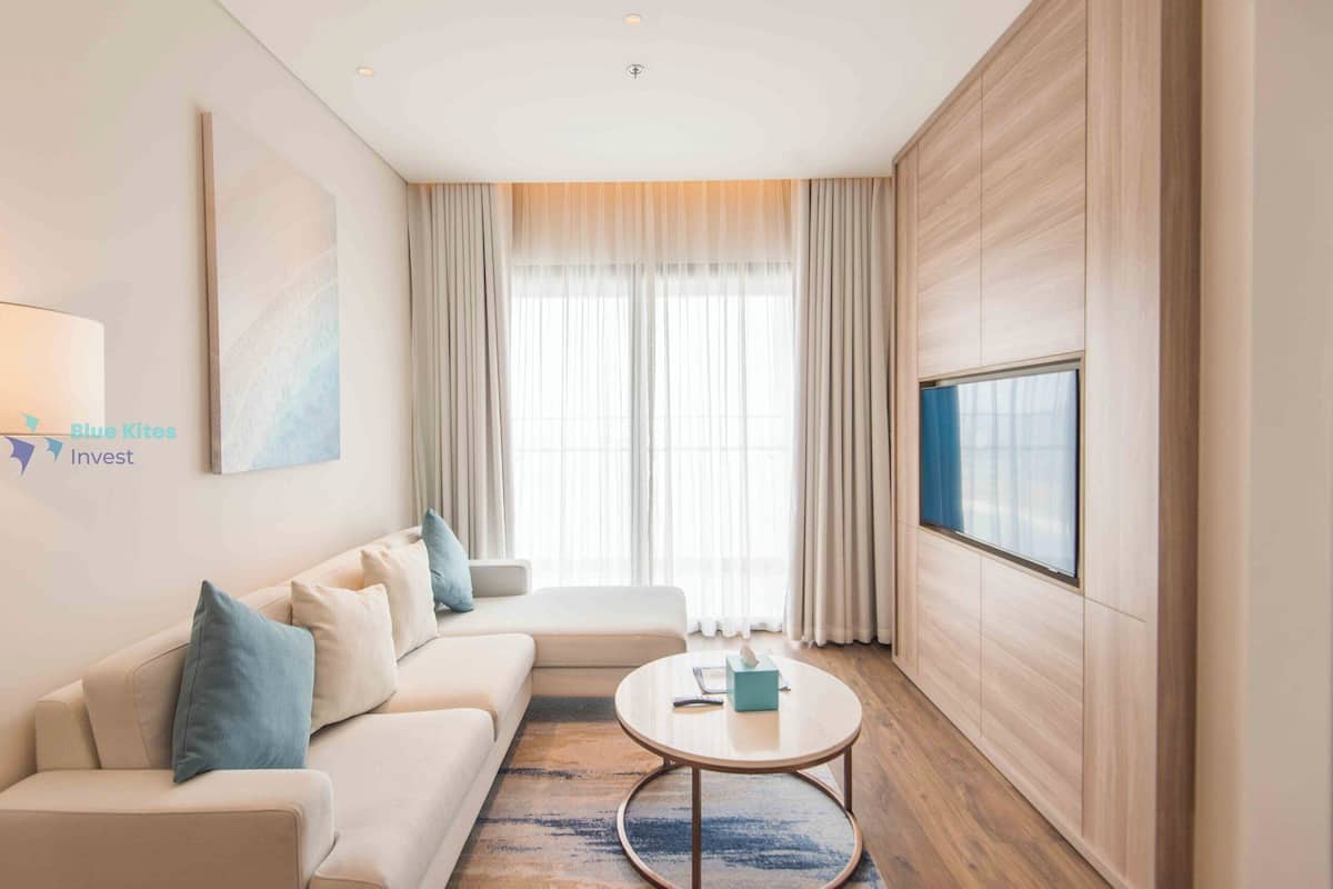 Une chambre d’hôtel moderne avec un canapé, une table basse ronde et un téléviseur fixé au mur.