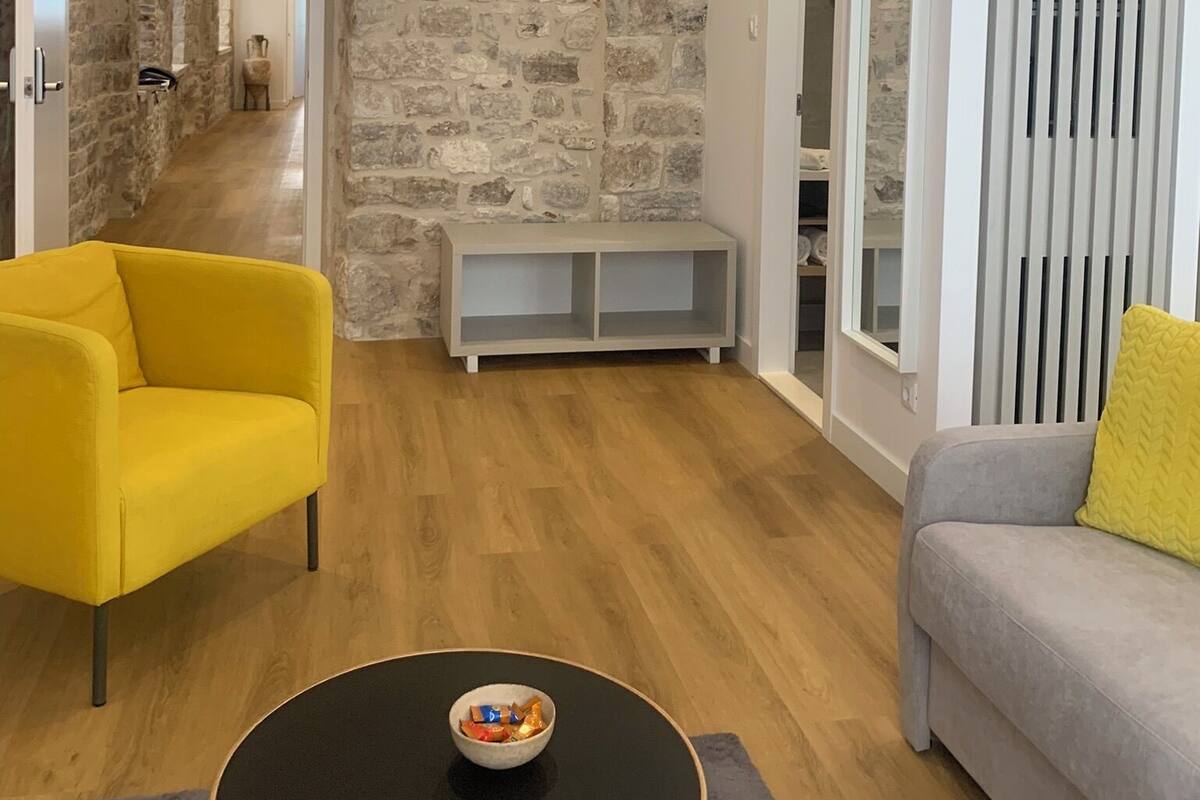 Ein modernes Wohnzimmer mit einer Steinwand, einem gelben Sessel, einem grauen Sofa und einem schwarzen Couchtisch.