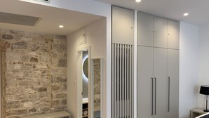 A modern interior with a stone wall, a bench, grey wardrobes, and a yellow cushion. - Priuli Heritage Suites (Split)