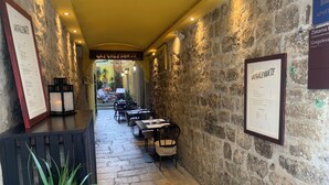 A narrow corridor with stone walls, a reception desk, and outdoor seating. - Priuli Heritage Suites (Split)