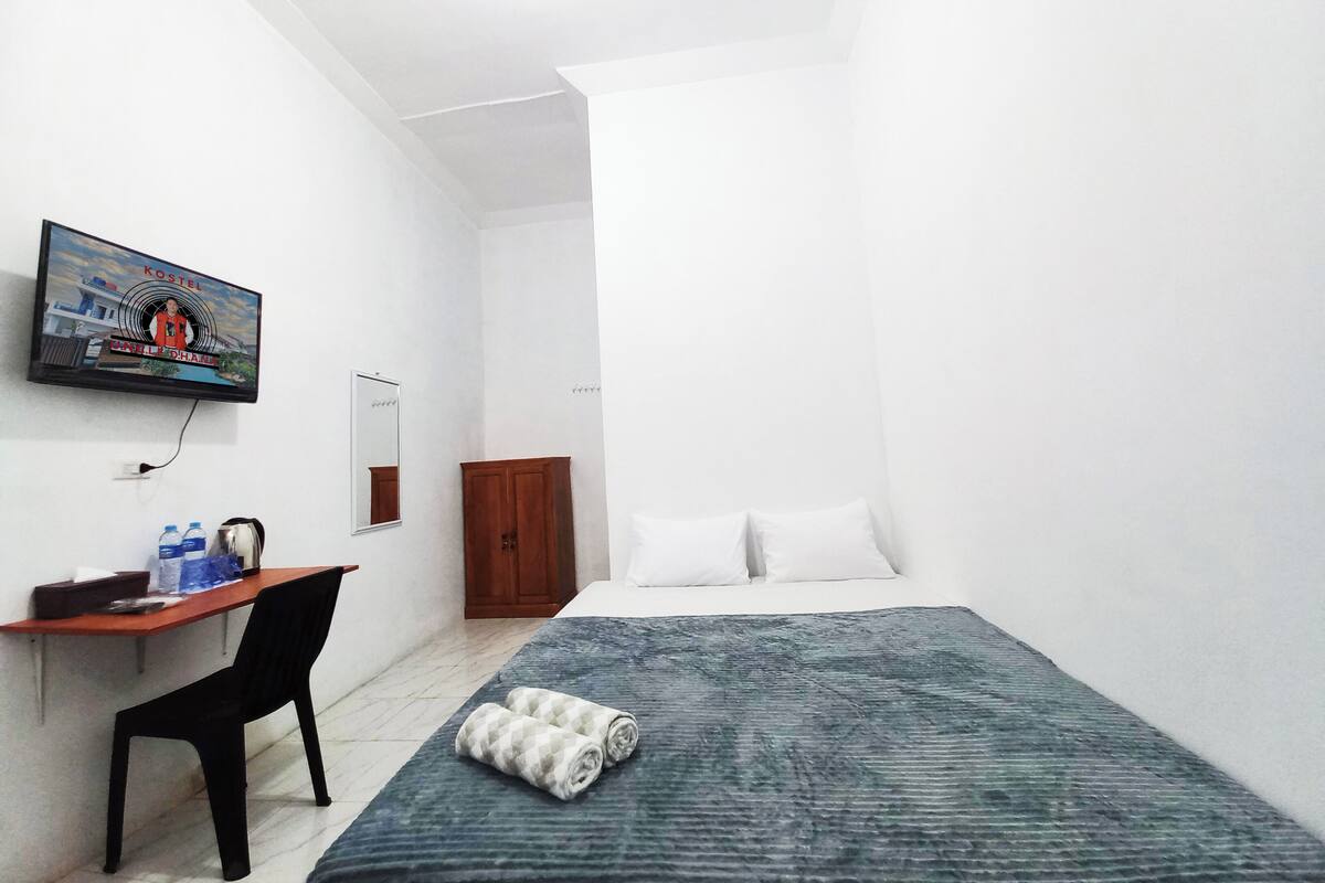 A small, clean room with a bed, a desk, a chair, a TV mounted on the wall, and a wardrobe.