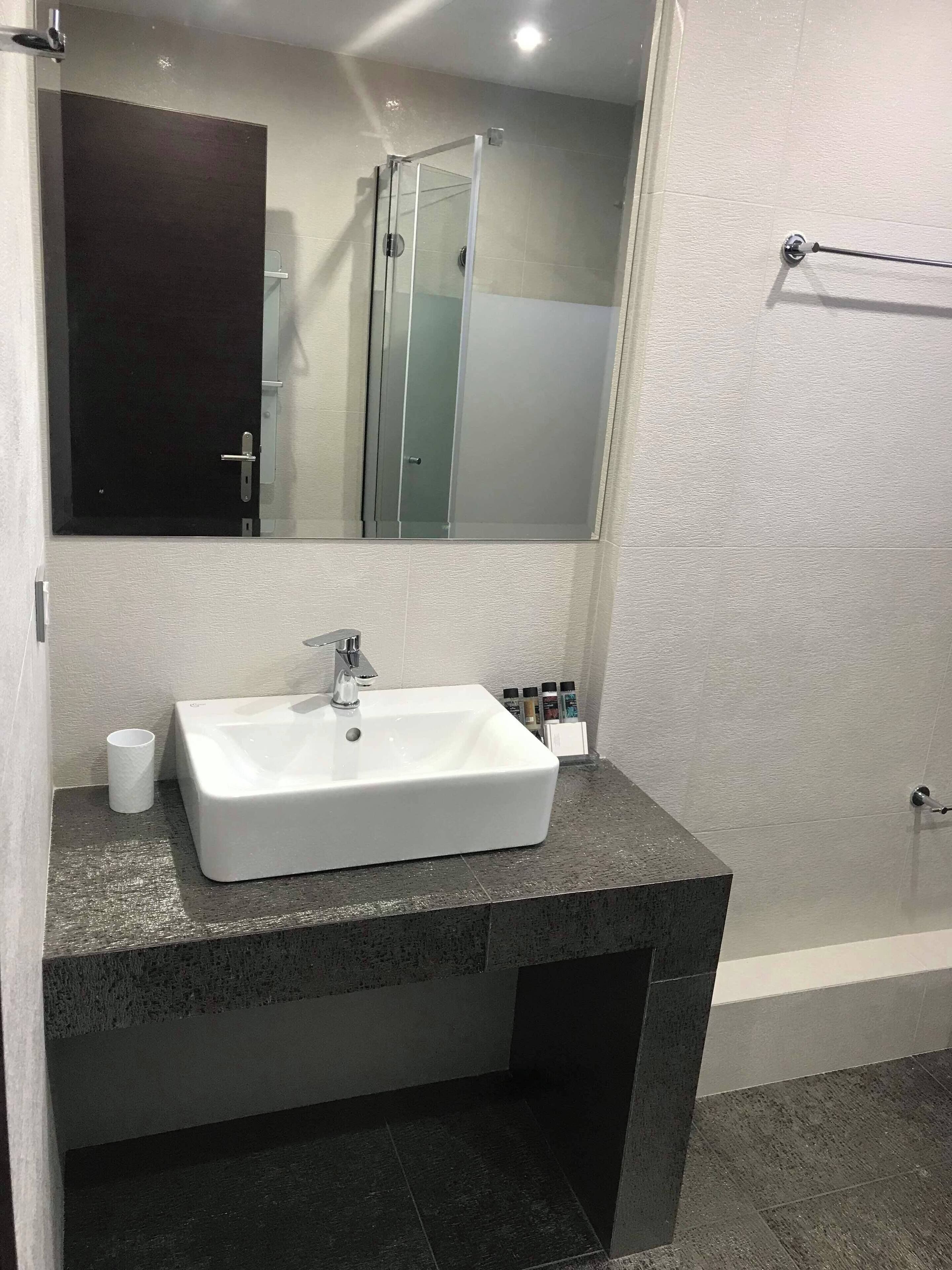 Un baño moderno con lavamanos blanco, encimera oscura y cabina de ducha con mampara de vidrio.