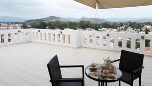 Una terraza con una mesa lista para el té, barandas blancas y vistas a colinas distantes.