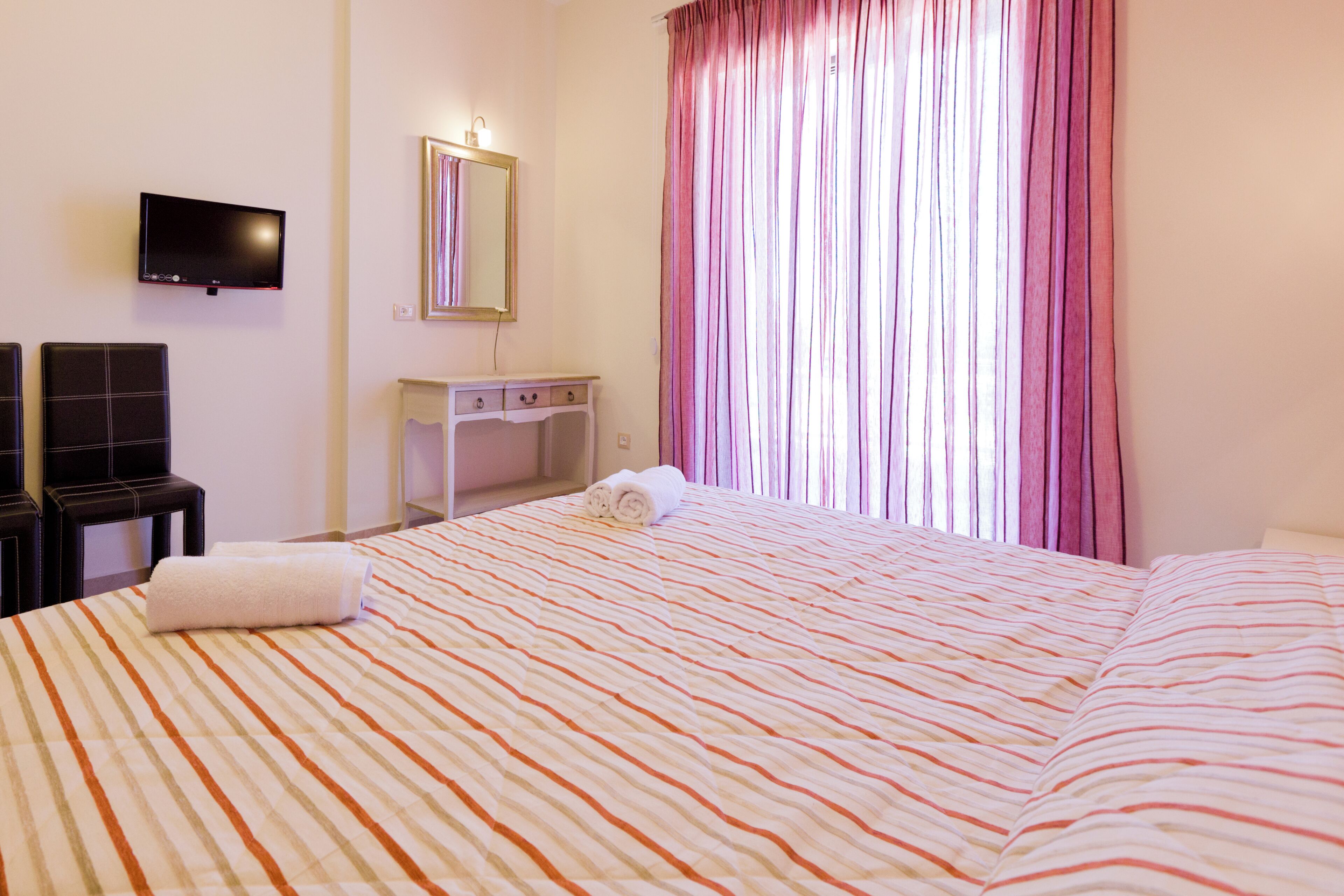 Une chambre d’hôtel avec un lit, une télévision, un bureau et une fenêtre avec des rideaux.