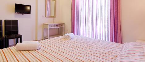 Une chambre d’hôtel avec un lit, une télévision, un bureau et une fenêtre avec des rideaux.