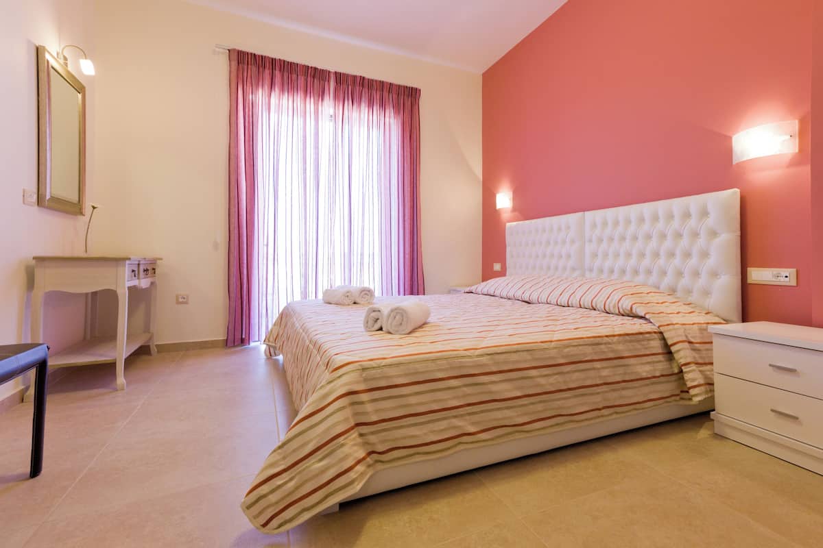 A bedroom with a bed, a bedside table, a mirror, and a window with curtains.
