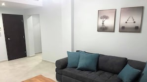 Una sala moderna con un sofá seccional gris oscuro, cojines verde azulado y una mesa de centro de madera. Hay dos obras de arte enmarcadas en la pared.
