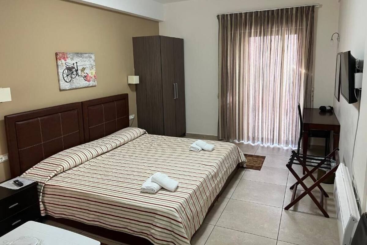 A hotel room with a large bed, a wardrobe, a desk with a chair, a television, and a window with curtains.
