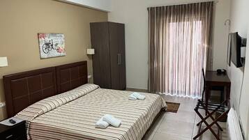 Habitación de hotel con una cama grande, un armario, un escritorio con silla, un televisor y una ventana con cortinas.