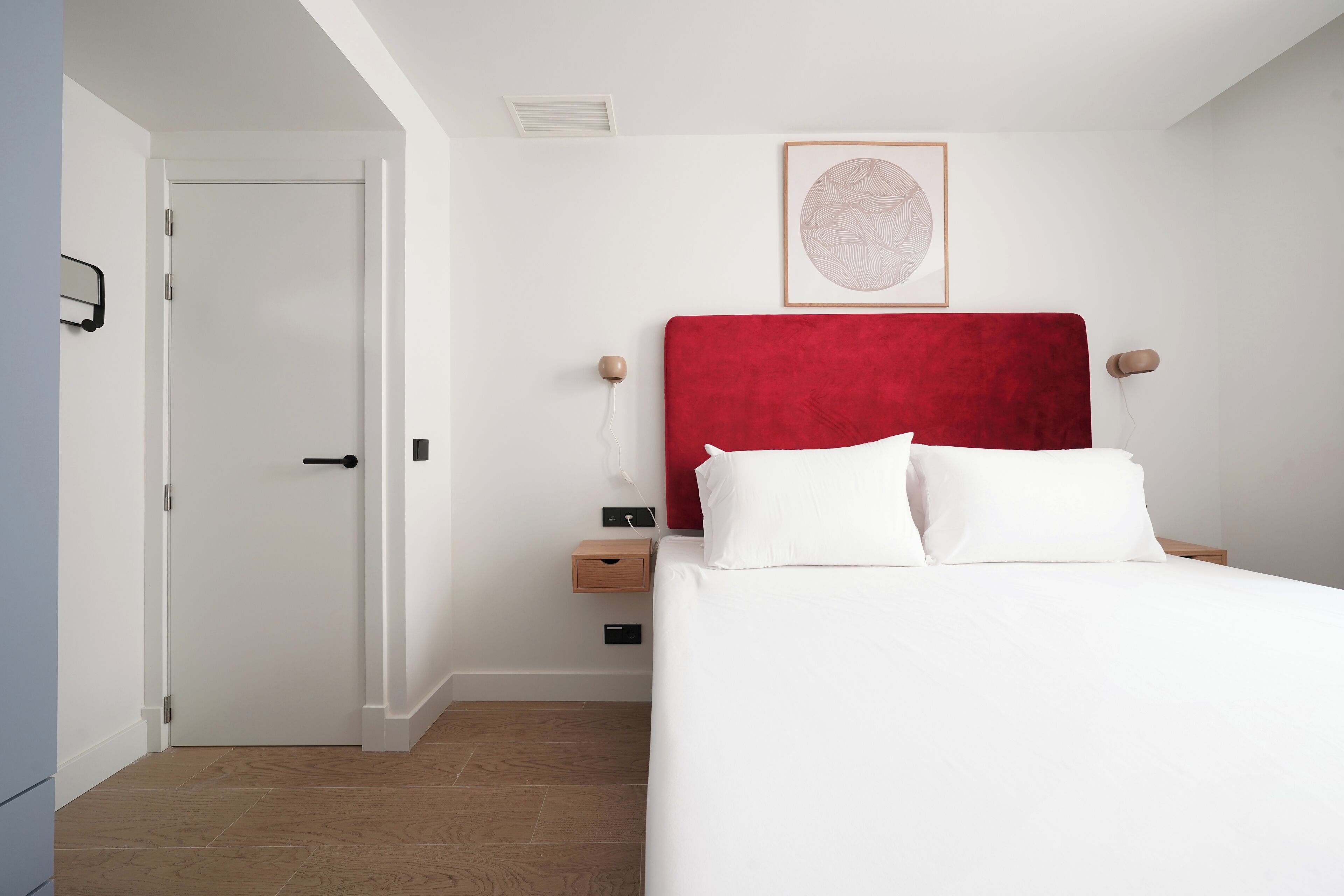 A bedroom with a white bed, red headboard, and a framed picture on the wall.
